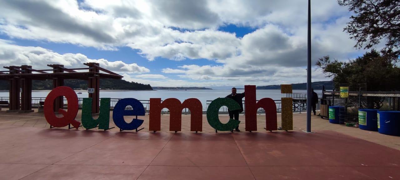 Imagen del nombre de Quemchi tallado en madera con fondo de mar